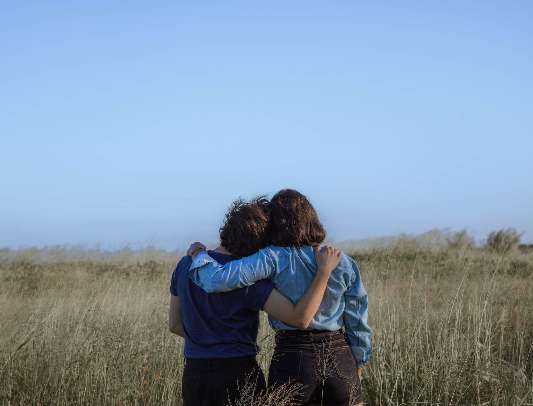 anonymous female friends embracing on spacious meadow