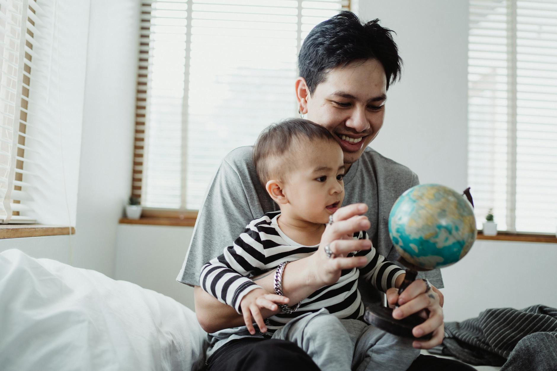 man showing globe to baby son in a bedroom