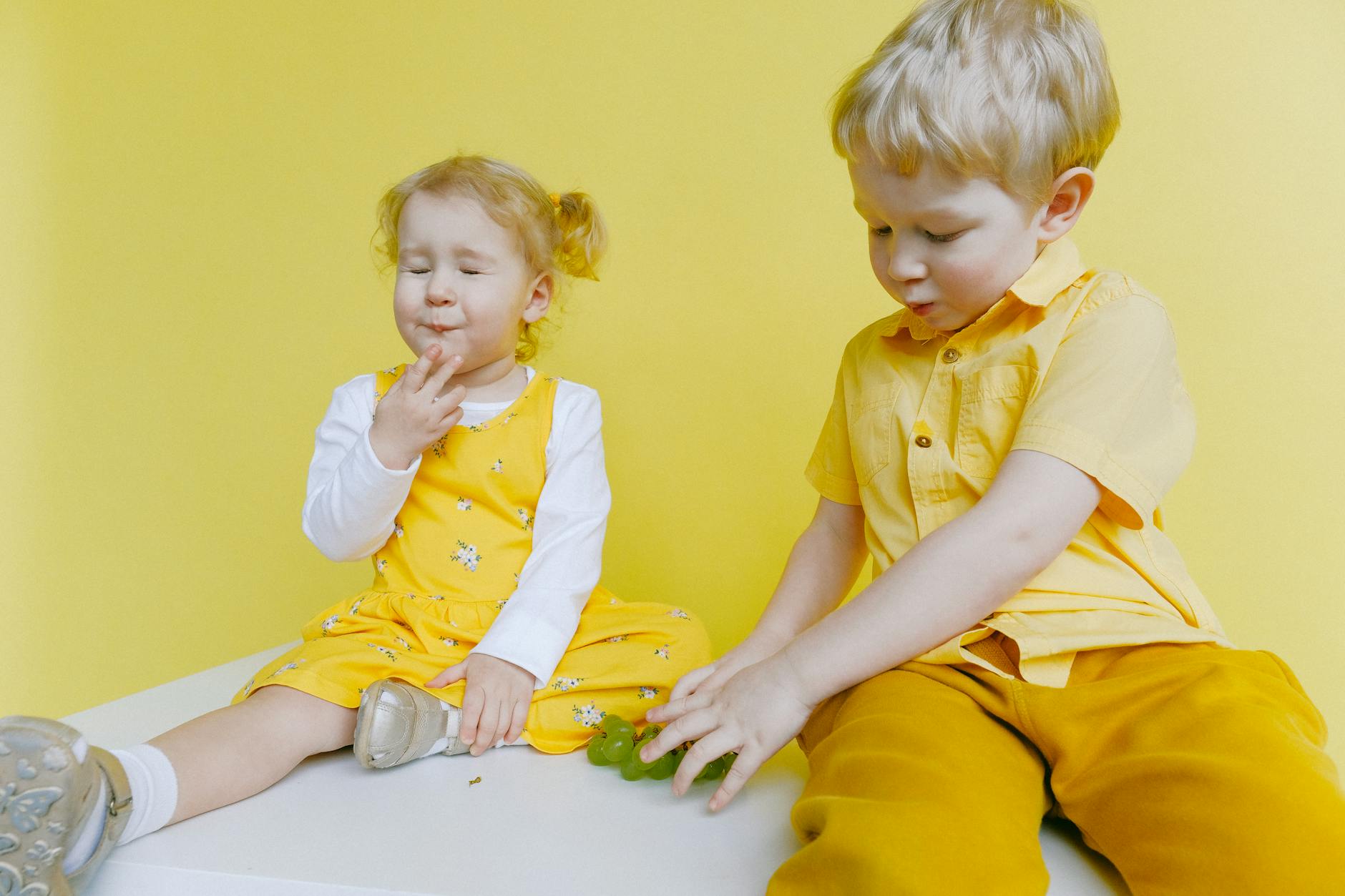 toddlers sitting on white table while eating green grapes