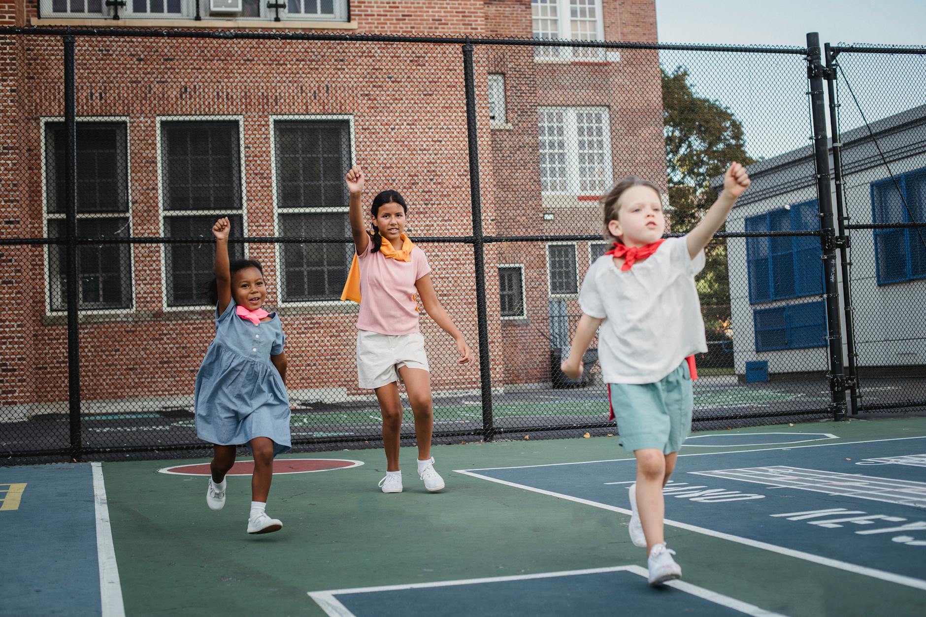 little girls playing superheros outdoors on a court in city