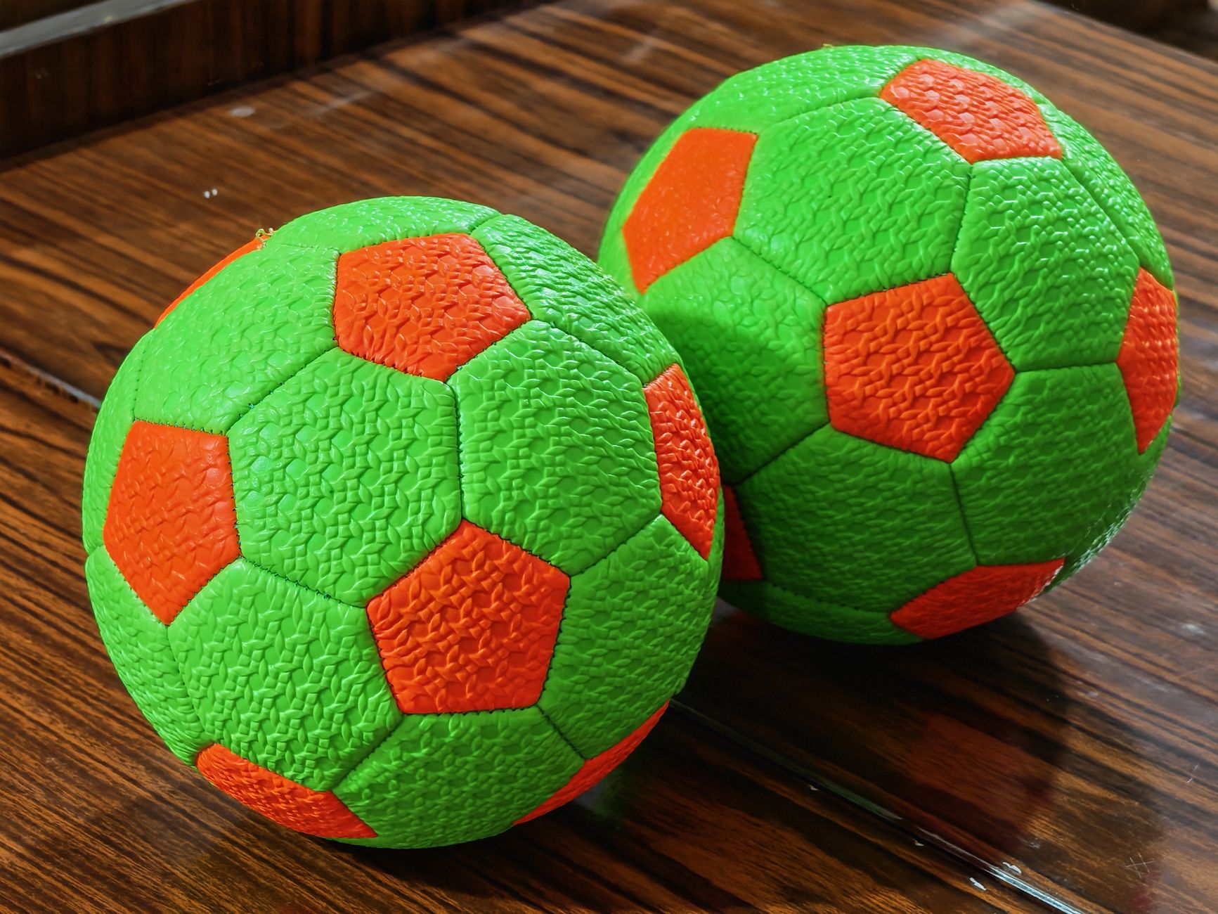 bright green and orange soccer balls on wooden floor
