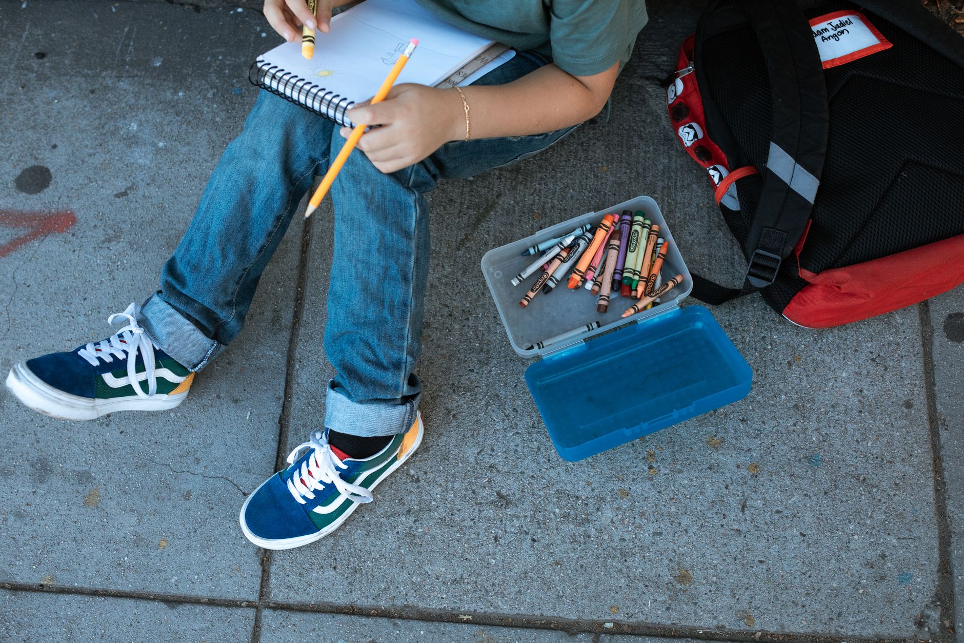 child in blue denim jeans and colorful sneakers sitting on floor coloring on sketchpad