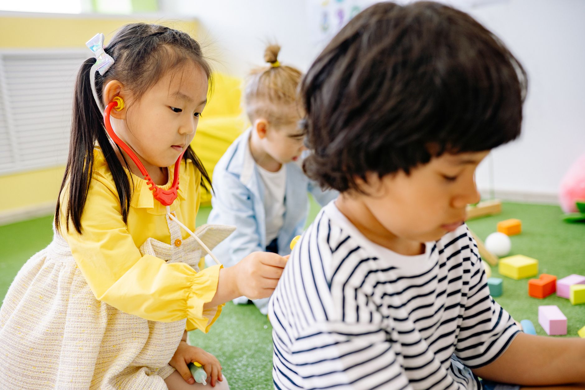 girl in yellow dress playing doctor to her classmate